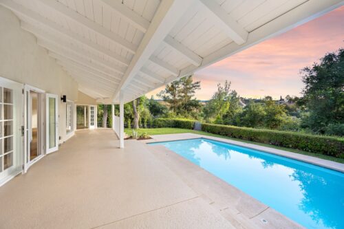 backyard pool at sunset with large balcony and greenery surrounding